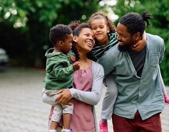 A family of four is standing outside with a car in the background.