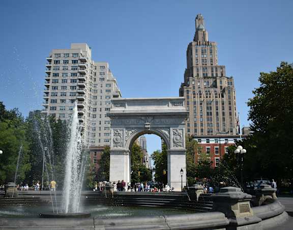 A fountain in front of a large archway and buildings.