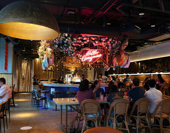 A restaurant with people sitting at tables and a neon sign that says "Happy Hour".