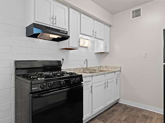 A black stove in a kitchen with white cabinets and a marble countertop.