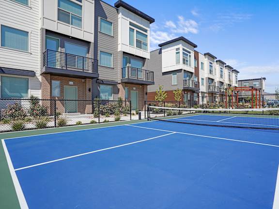 A tennis court is surrounded by apartment buildings.