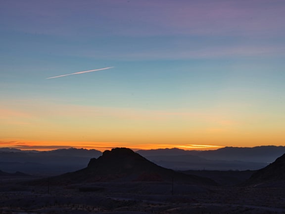A mountain range under a sunset with a contrail in the sky.