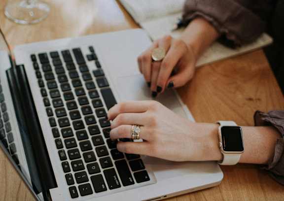 A person in a yellow sweater is typing on a laptop.