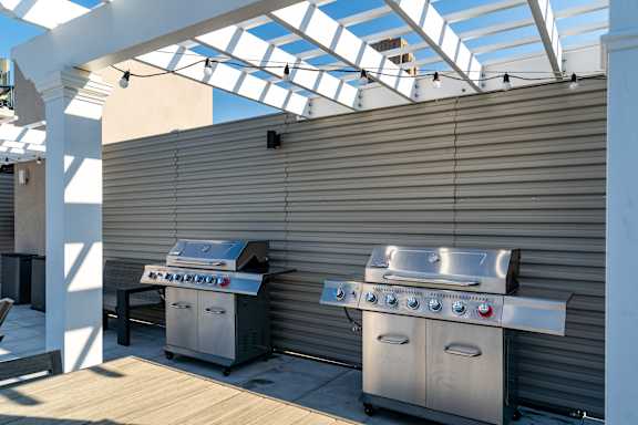 Two grills are on a patio under a white pergola.