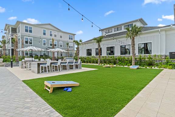 A patio area with a table and chairs is surrounded by a grassy area and a building in the background.