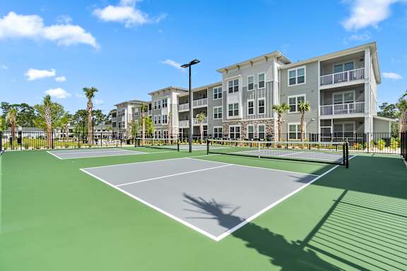 A tennis court in front of a building with palm trees.
