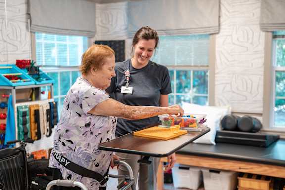 an older woman painting a picture at a table with other people painting on canvases