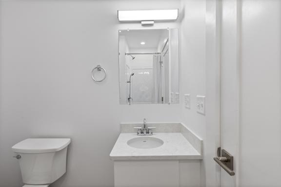 A white bathroom with a toilet, sink and mirror.