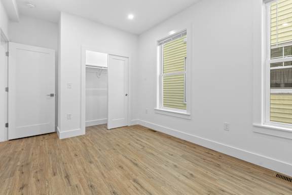 A room with white walls and wooden flooring with a window on the right side.