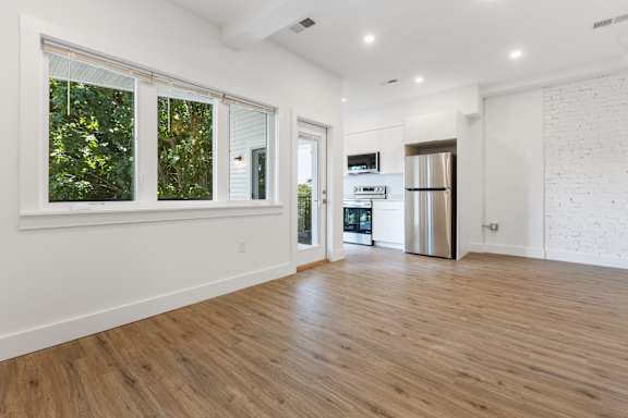 A spacious room with wooden flooring and a kitchen area in the background.