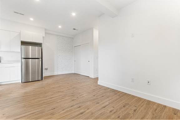 A kitchen with a stainless steel refrigerator and wooden flooring.