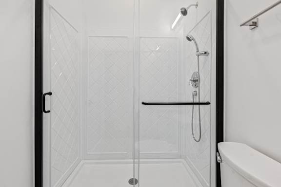 A white tiled shower with a glass door and a black handle.