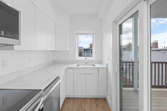 A kitchen with white cabinets and a window overlooking a building.
