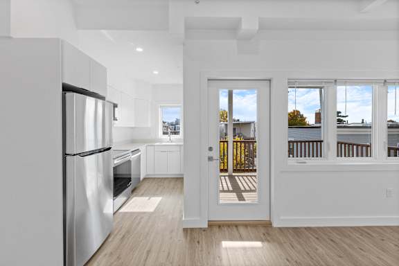 A modern kitchen with a refrigerator, oven, and a view of the outdoors through the door.