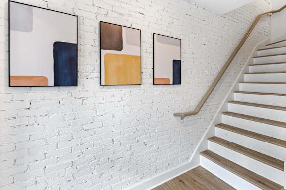 a white brick wall with three paintings on it and a staircase
