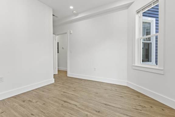 A room with white walls and wooden flooring with a window on the right side.
