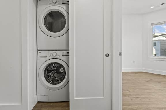A white door opens to a room with a washing machine in it.
