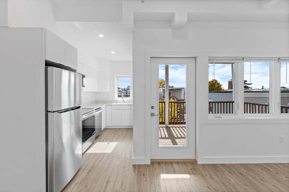 A modern kitchen with a refrigerator, oven, and a view of the outdoors through the door.