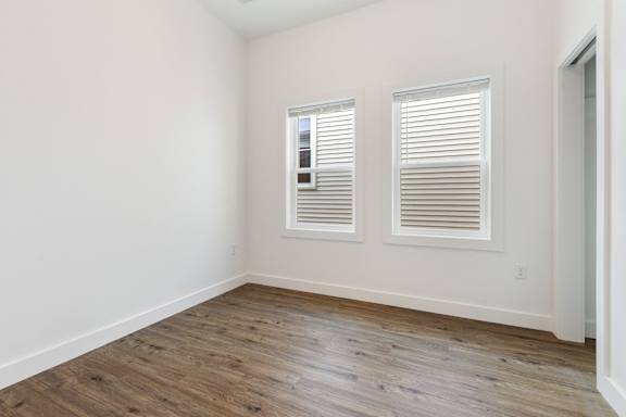 A room with wooden floors and two windows with blinds.