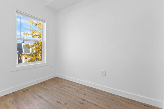 A room with a window showing a view of a house and trees.