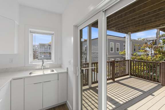 A small white kitchen with a sink and a wooden deck outside.