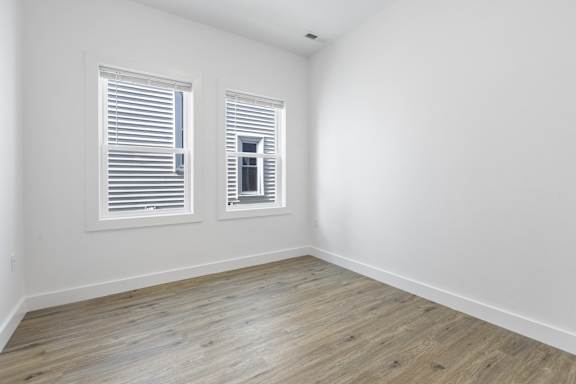 A room with wooden flooring and two windows.
