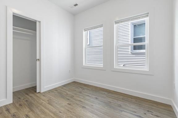 A room with a wooden floor and two windows with white blinds.