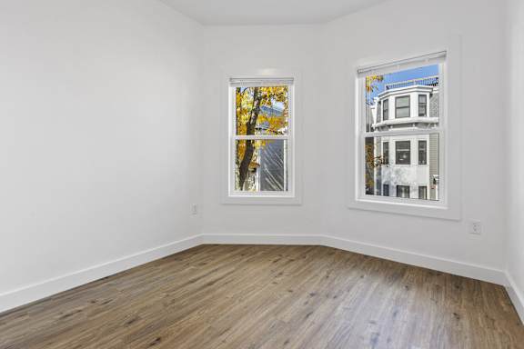 A room with two windows, one showing trees and the other a building.