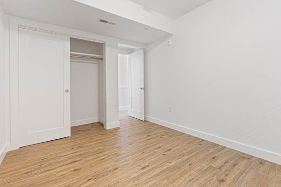 A room with white walls and wooden flooring with a door on the left and an open doorway on the right.