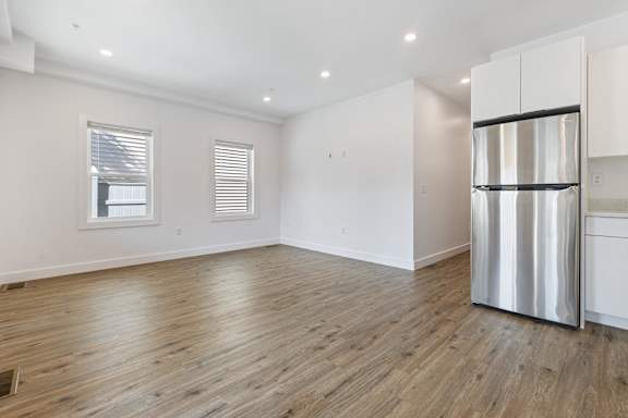 A room with a wooden floor and a stainless steel refrigerator.