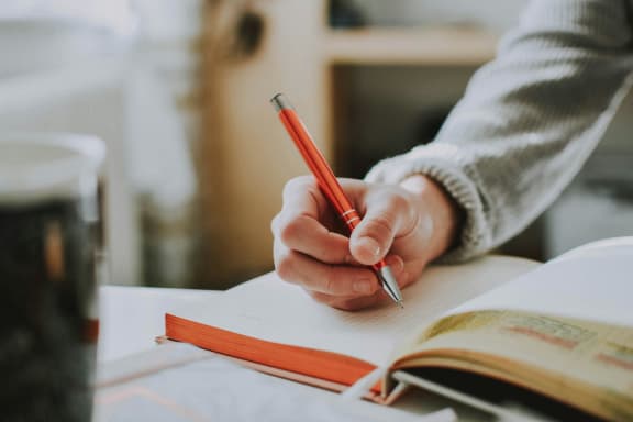a person writing in a book with a pen