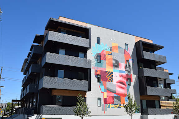 A large mural of a woman's face is on the side of a modern building.