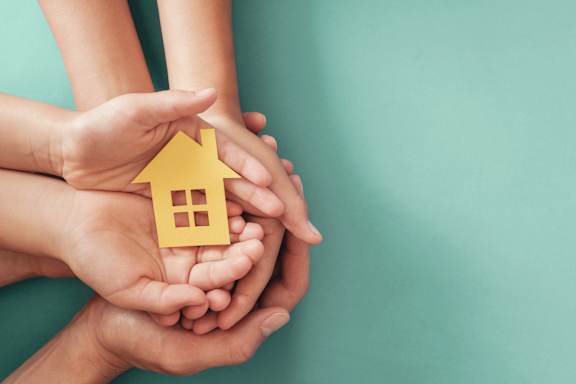 A group of hands holding a small yellow house.