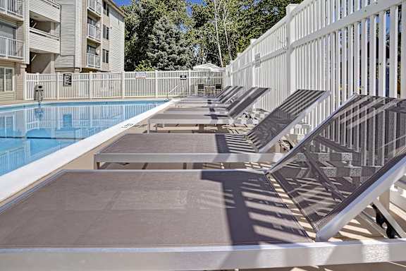 A row of sun loungers are on the edge of a pool.