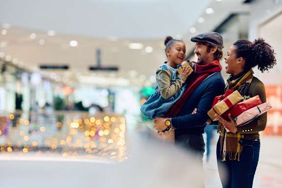 two women and a man standing in a shopping mall holding gifts