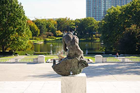 A sculpture of a lion is sitting on a pedestal in a park.