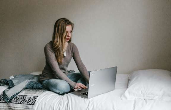 A woman is sitting on a bed using a laptop.