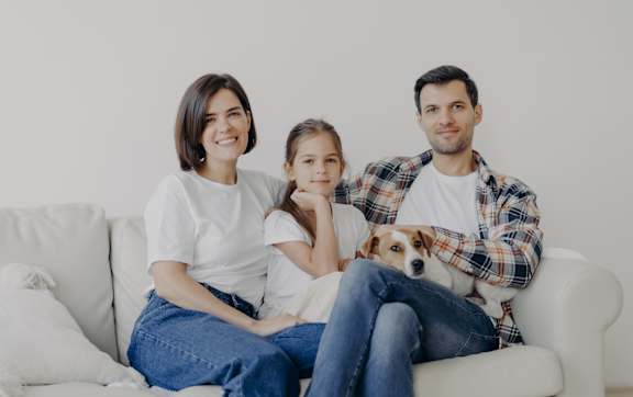 A family of four is sitting closely together on a couch.