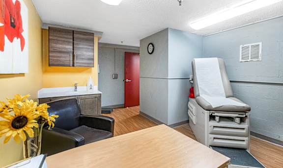 A hospital room with a bed, a chair, and a vase of sunflowers.