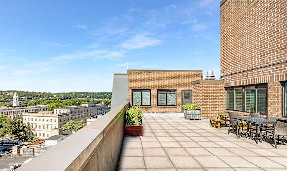 A rooftop patio with a table and chairs overlooks a cityscape.