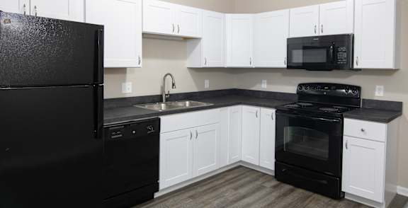A room with a black fridge and wooden flooring.