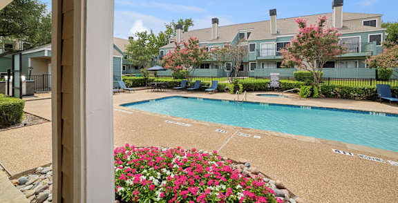 A pool surrounded by a flower bed and apartment buildings in the background.