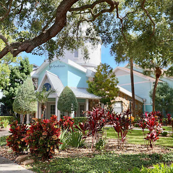A house with a blue roof and white trim is surrounded by greenery.