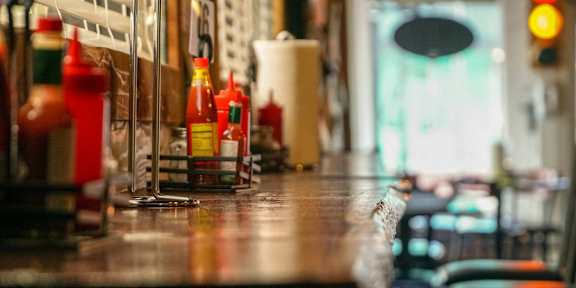 A row of condiment bottles are lined up on a bar.