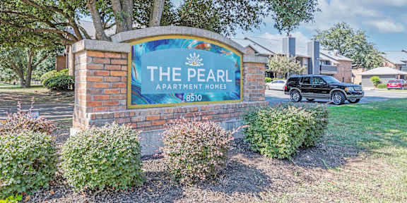 A sign for The Pearl Apartment Homes stands in front of a tree and shrubs.