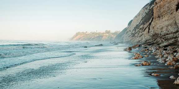 A beach with waves crashing onto the shore and a rocky cliff on the right side.