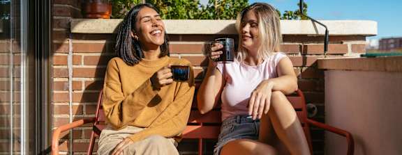 Two women sitting on a bench, one holding a phone.