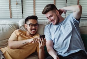 two men sitting on a couch looking at a cell phone