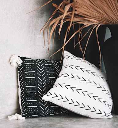a black and white pillow on a shelf next to a black vase with a plant