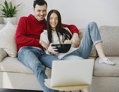 a man and a woman sitting on a couch with a laptop